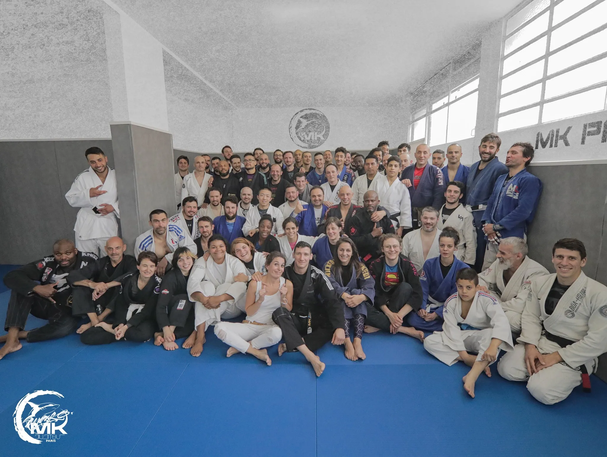 Les pratiquants de la MKTeam réunis sur les tatamis bleus du dojo, logo MK au mur